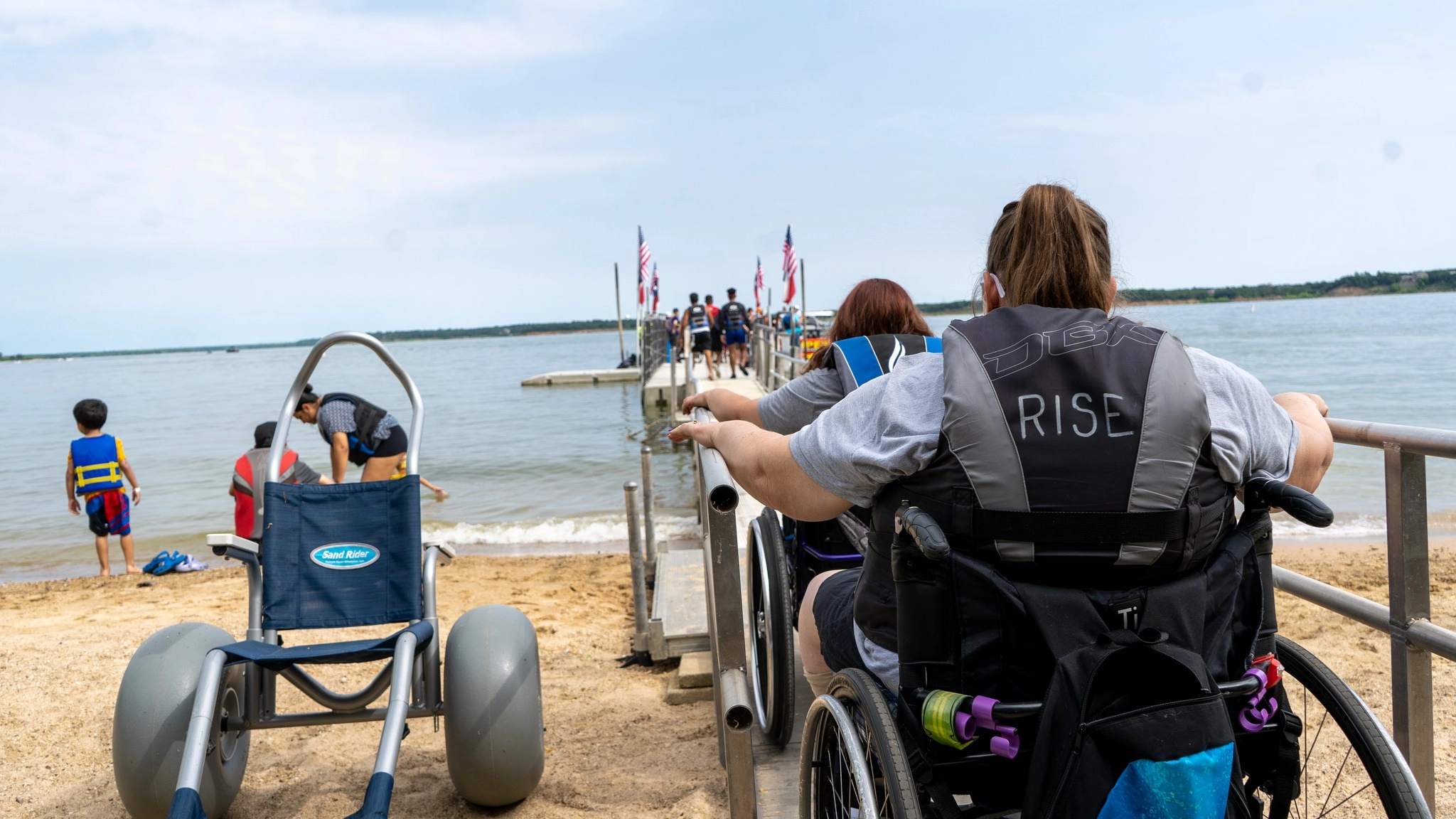 Two wheelchair users move down an accessible ramp toward the lake at a RISE program.