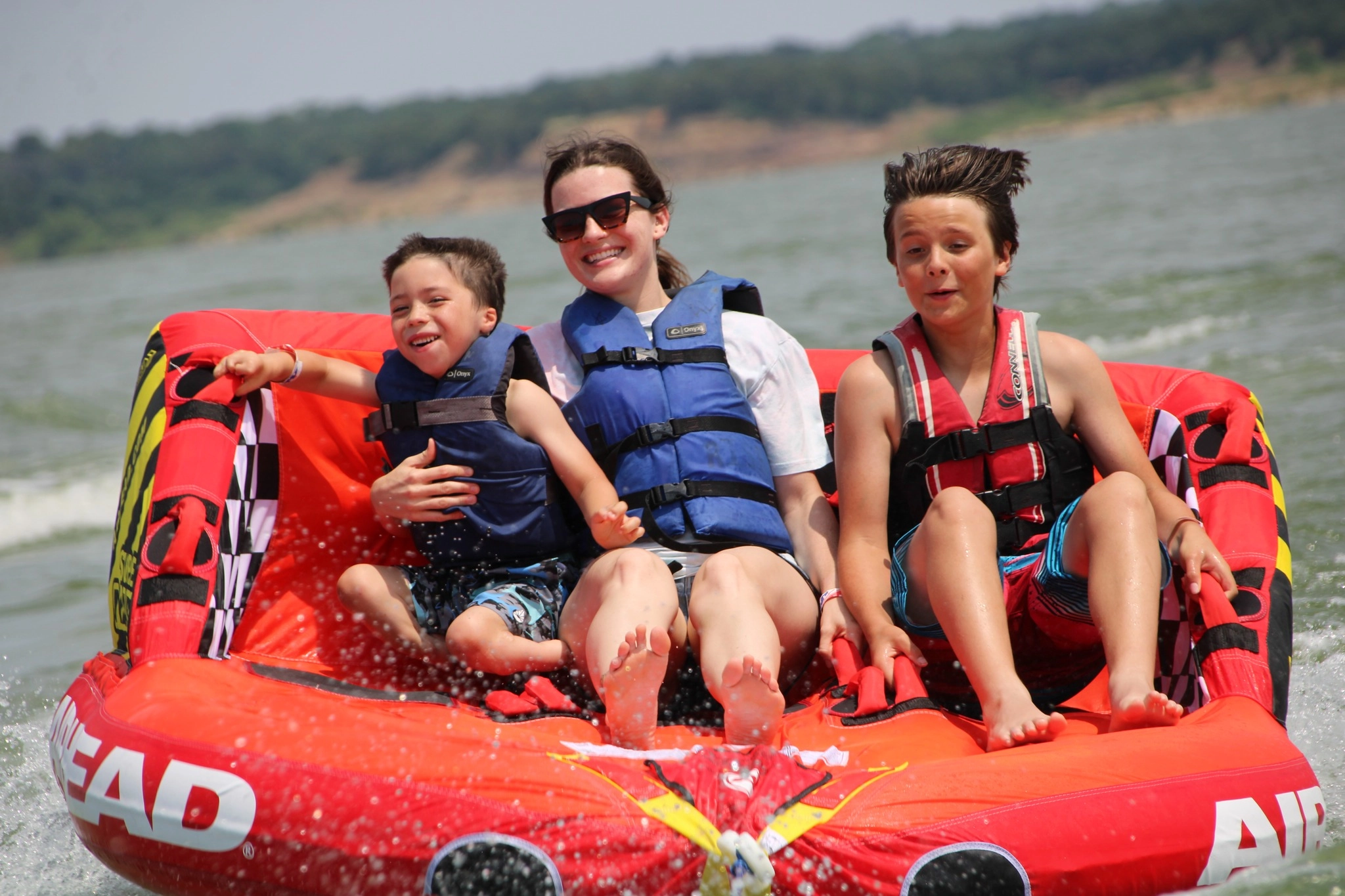An adult rides a tube with two children at a RISE lake program.